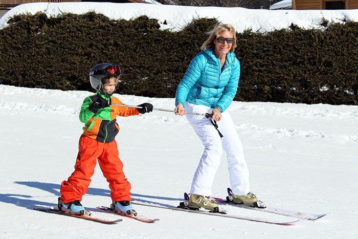 une mamie apprend à son petit fils à skier grâce à la technique du bâton.