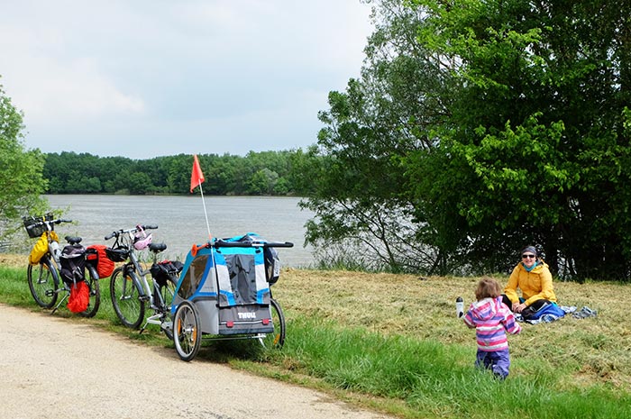 Pique-nique sur l'herbe en famille à côte des vélos et de la carriole, en bord de
