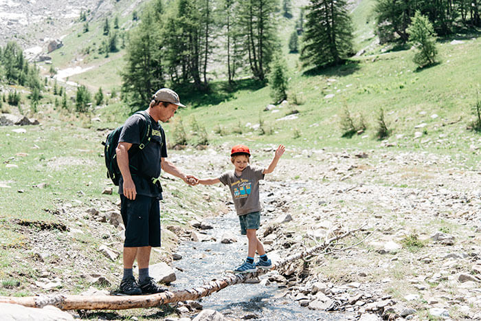 papa et son enfant traversent un torrent durant une randonnée en famille dans le val d'Allos en Provence Alpes Côte d'Azur