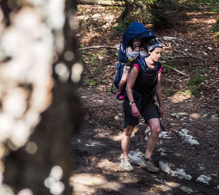 fille portée sur le dos de sa maman avec le nouveau porte bébé Deuter Kid Comfort Pro en promenade en forêt