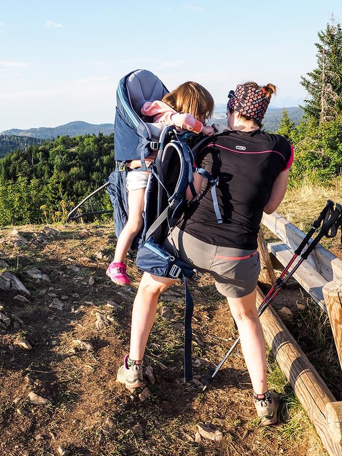 une maman charge le porte bébé Deuter Kid Comfort Pro avec sa fille au moment de partir en balade