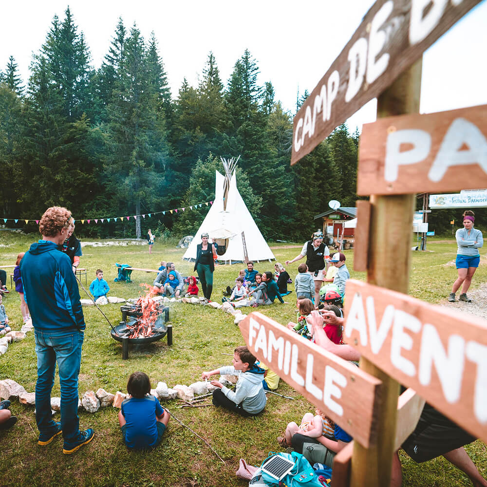 Familles autour d'un feu de camp en montagne devant un tipi.